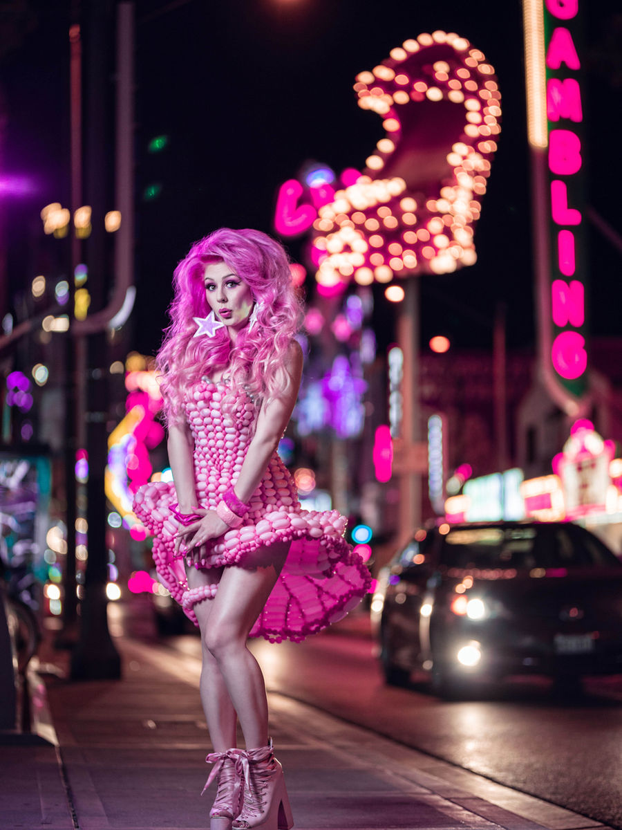 Model wearing a full pink balloon dress and headpiece standing under the neon signs of downtown Las Vegas.