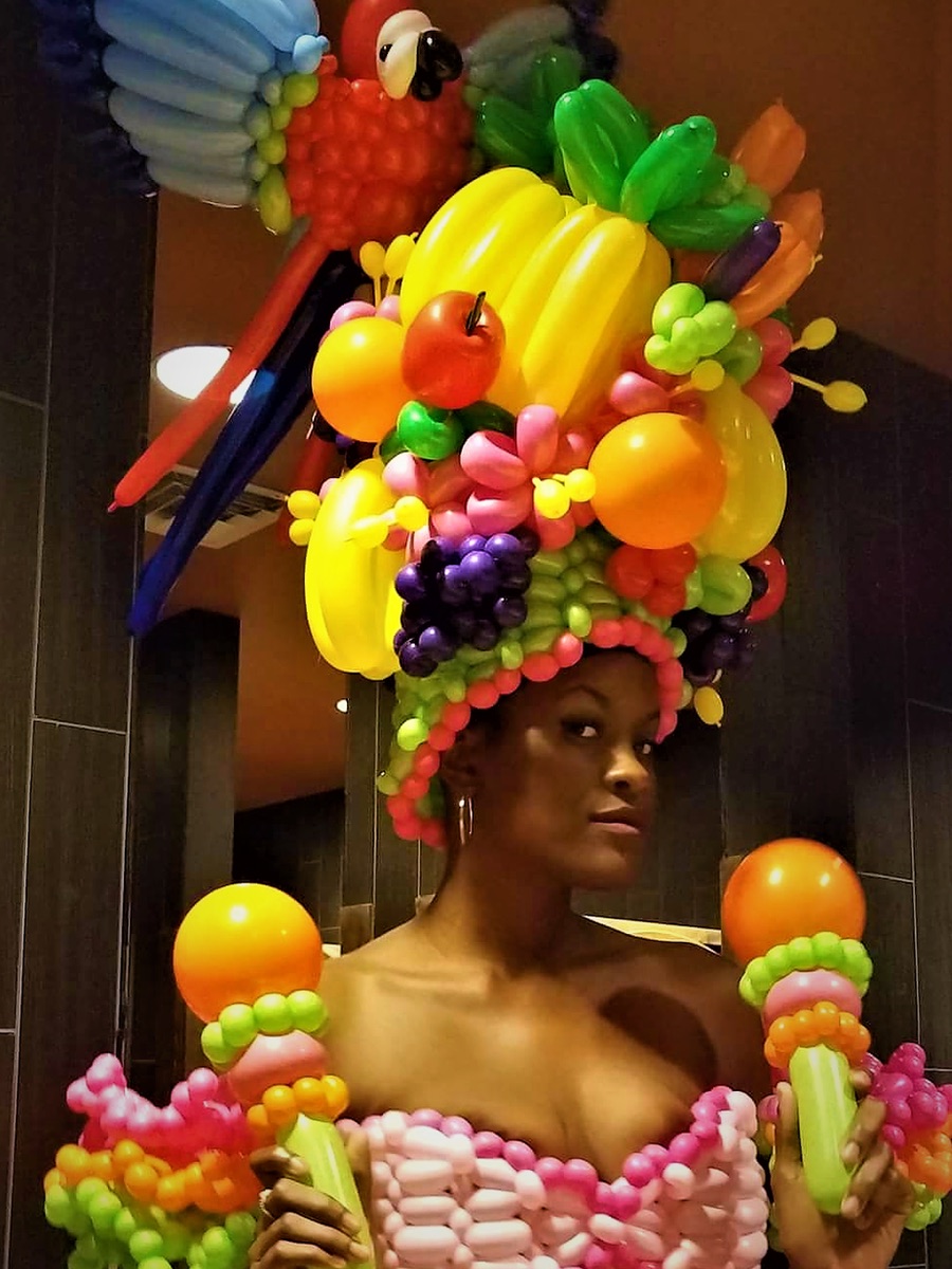 Model in a balloon gown with an elaborate tropical fruit and parrot balloon headdress.